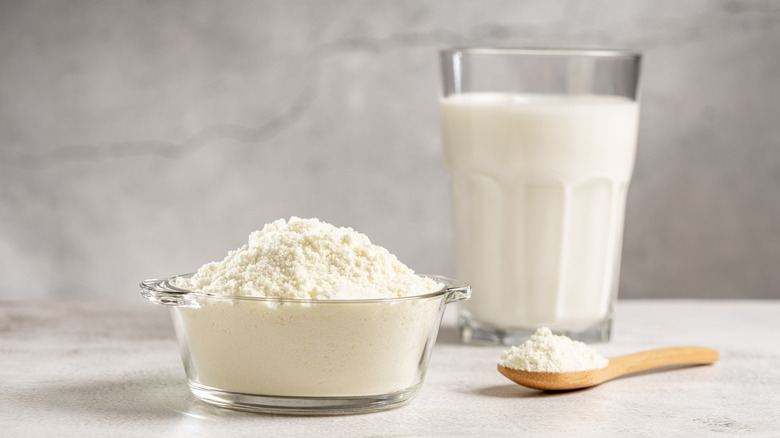 Bowl and spoon of powdered milk next to a glass of milk