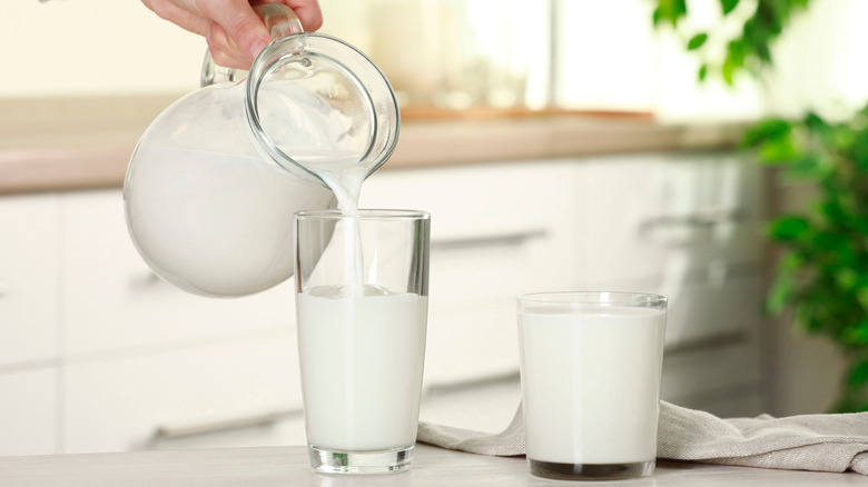 Hand pouring two glasses of milk from pitcher