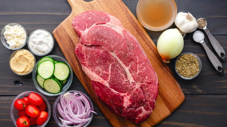 A raw piece of chuck roast on a wooden cutting board, surrounded by ingredients.