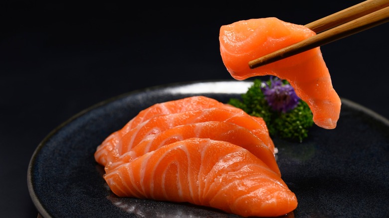 Salmon sashimi on a black plate, one piece picked up with chopsticks.