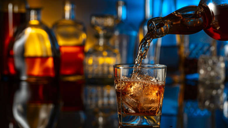 Whiskey being poured into a glass inside a dark bar.