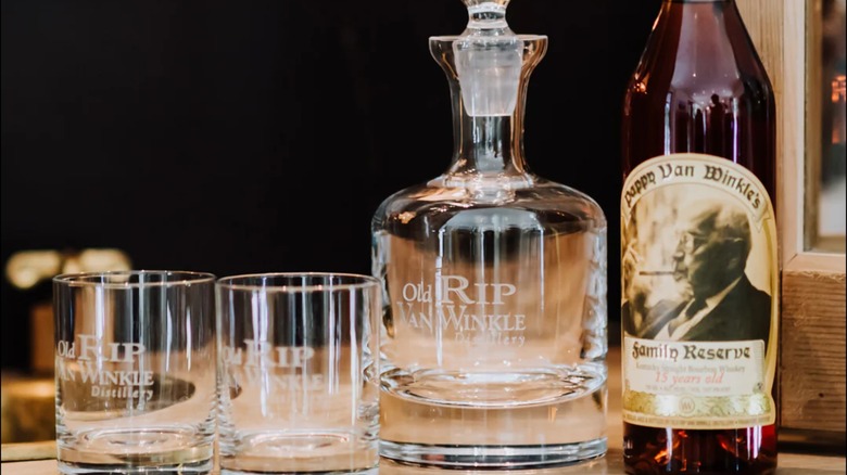 A bottle of Pappy Van Winkle's bourbon whiskey next to a branded decanter and two glasses