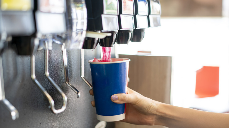 Someone using a soda fountain to fill a blue cup with a red soda