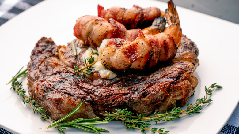 Close up of a large piece of steak and lobster sitting on top of it with garnish