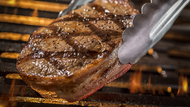 steak in tongs over grill