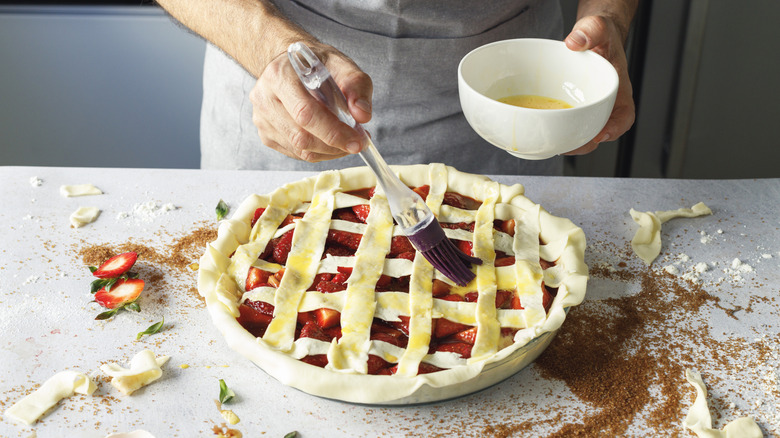 Person's hand brushing fruit pie with egg wash