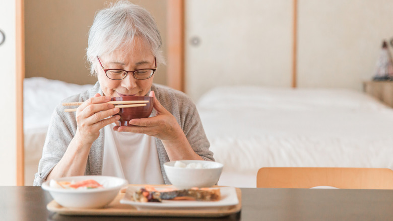 Elderly woman drinking bowl of miso soup