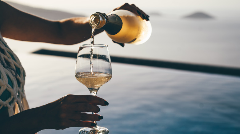 woman pouring white wine by the ocean