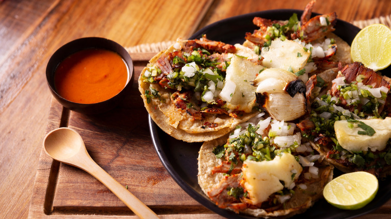 A platter of Al Pastor tacos sit on a plate next to salsa