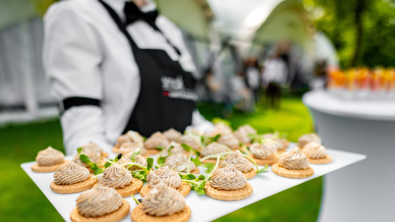 Canapés topped with whipped pâté being served on a platter by a waitress