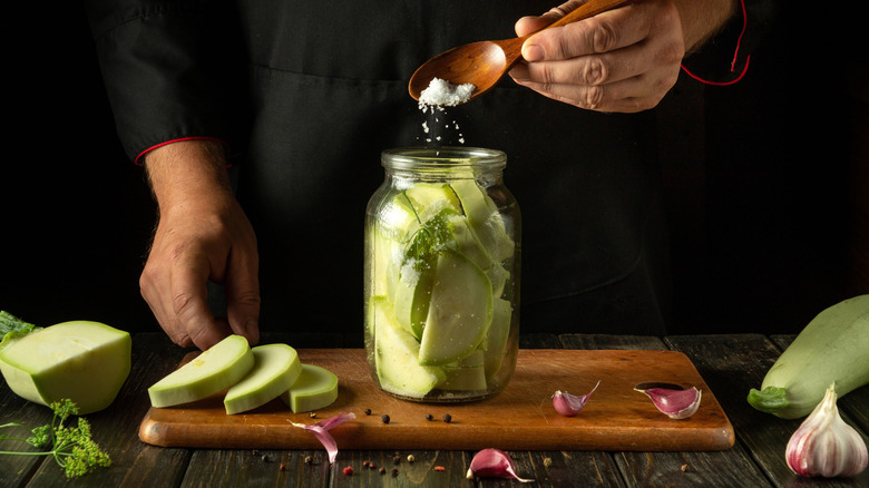 person pouring spoonful of canning salt into jar of pickles