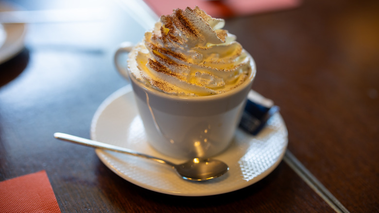 White cup and saucer with spoon and large pile of whipped cream on top