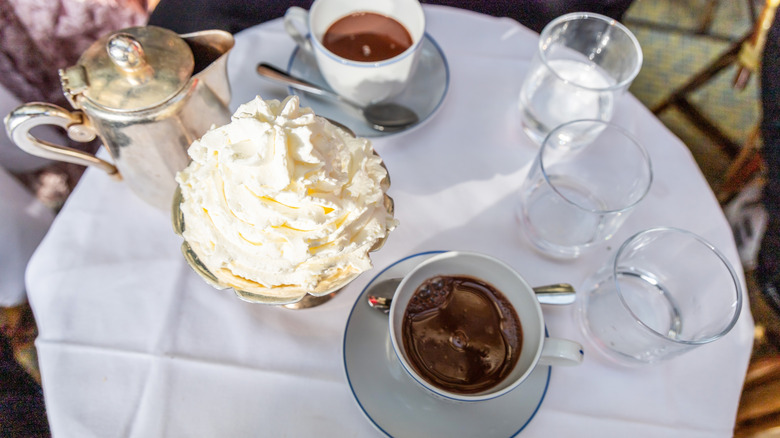 Cafe table with two cups of dark hot chocolate and dish of whipped cream