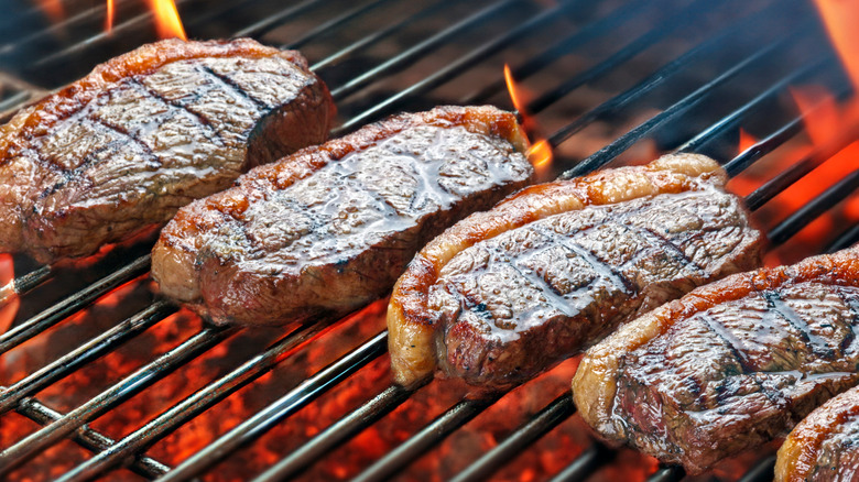 Charred cuts of steak cooking on an open-fire grill