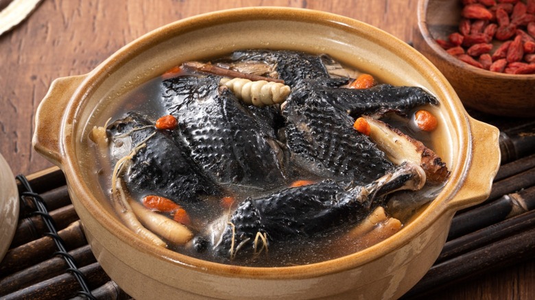 A silkie chicken, cooking in broth with vegetables.