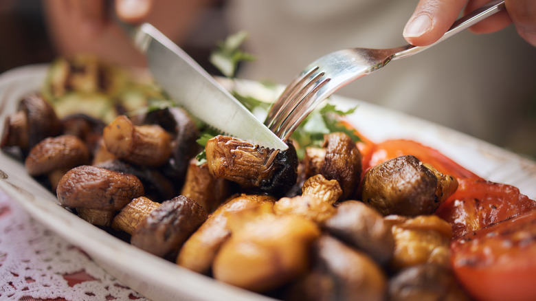 Hands cutting roasted mushroom dish at restaurant