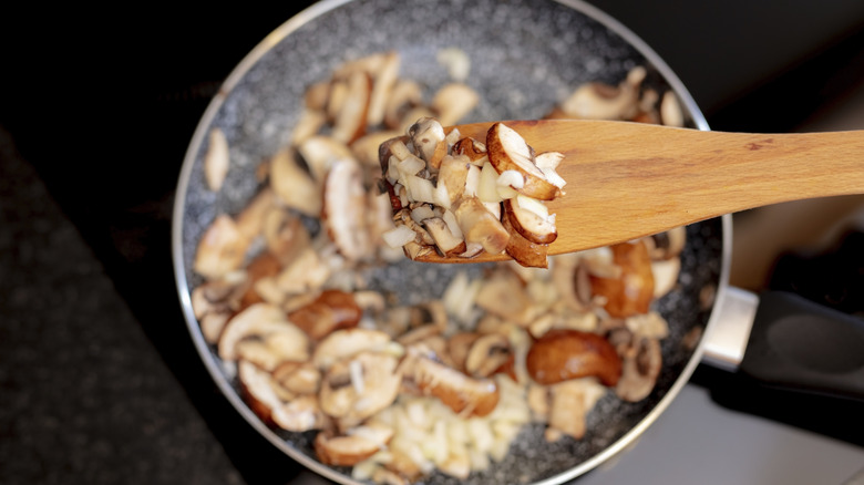 A wooden spoon holding mushrooms over saute pan