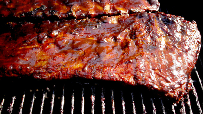 A slab of ribs covered in barbecue sauce cooking on a grill.