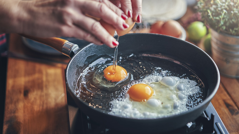 a woman cracking eggs into a pan of hot oil