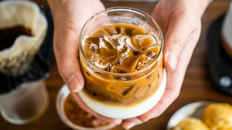 A glass cup of iced Thai coffee held by a man.