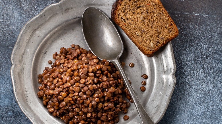 Brown lentils and a slice from an unidentified loaf on a plate with a spoon