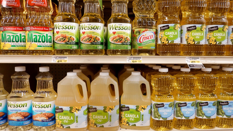 A grocery store shelf with different brands of canola and vegetable oils