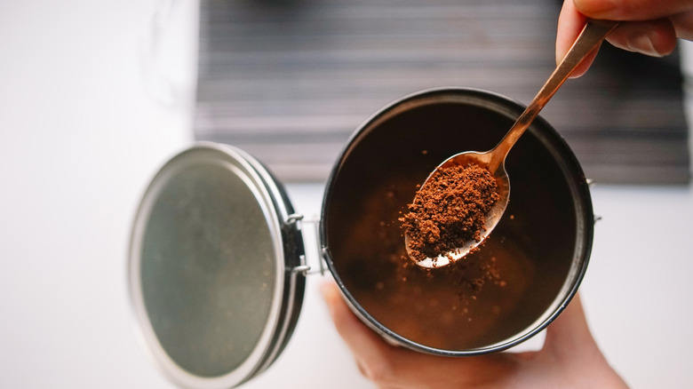 A person using a spoon to scoop coffee grinds from a jar