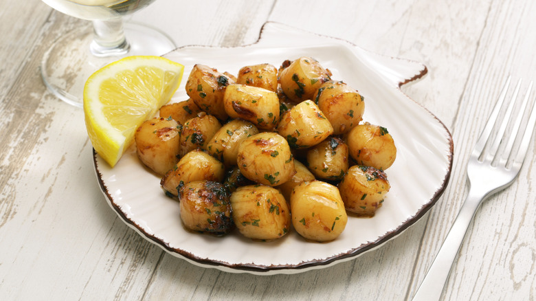 A small plate of bay scallops with a lemon wedge on the side