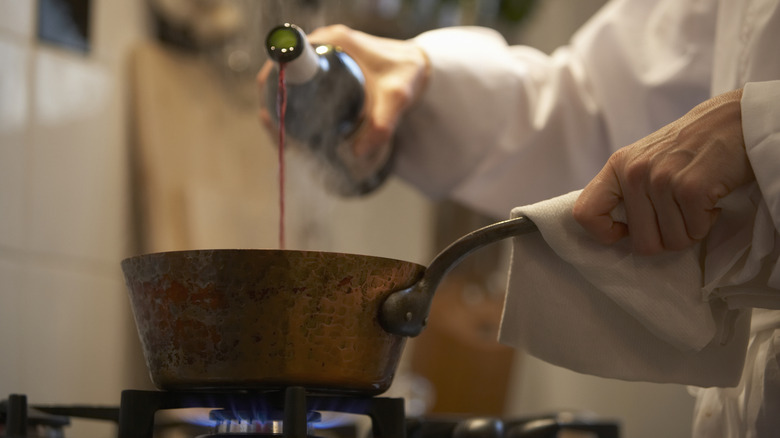 Person pouring red wine into a pot sitting on an open flame stove burner