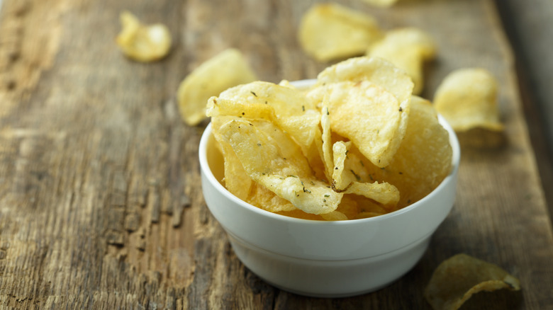 Small white bowl of kettle chips sitting on a wooden surface