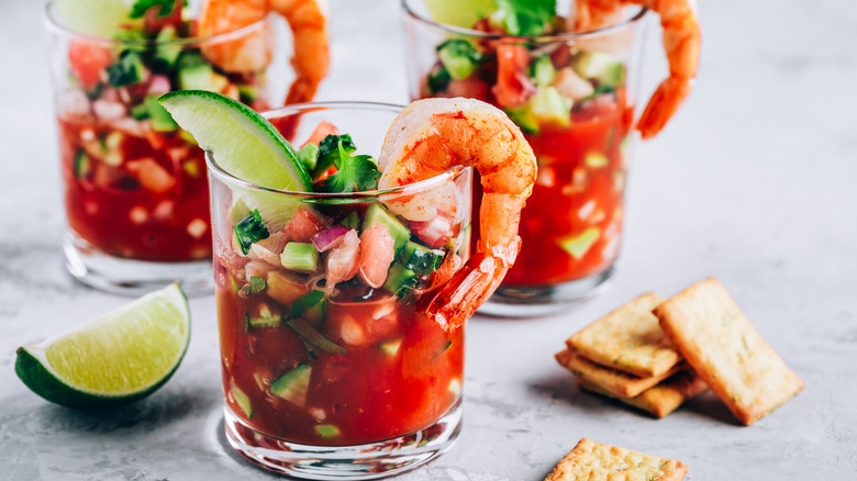 Three glasses of Mexican shrimp cocktail with lime wedge and crackers