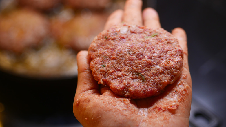 a hand holding out a formed raw beef patty