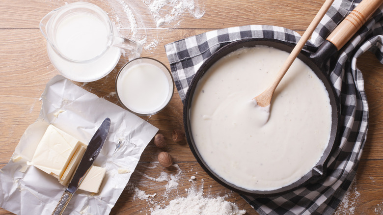 Pan of béchamel sauce surrounded by the ingredients to make it