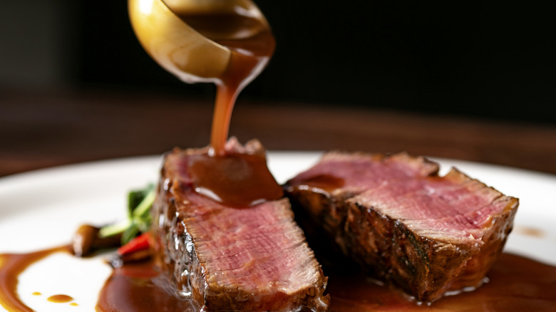 Demi-glace sauce being poured over filet mignon steak