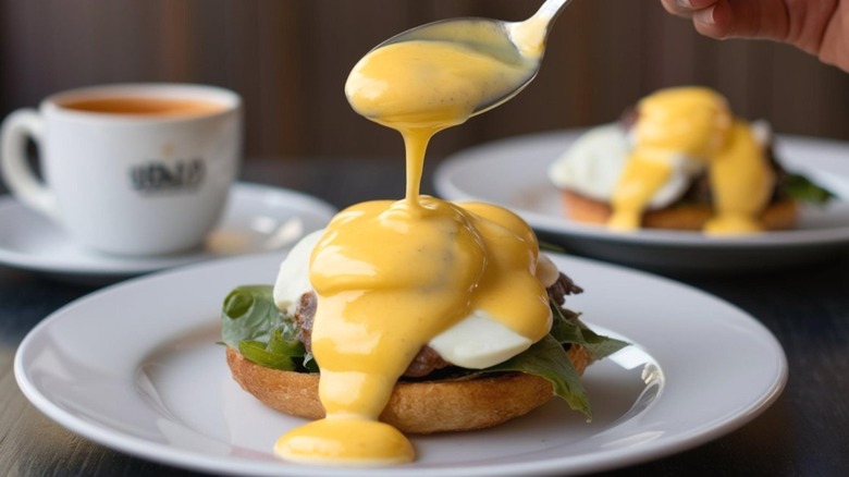 Hollandaise sauce being spooned over eggs benedict