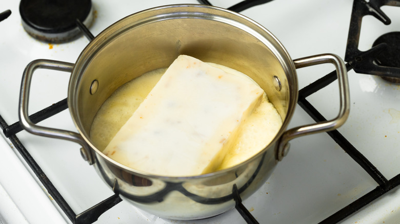 a block of frozen soup thawing in a pot on a gas stove