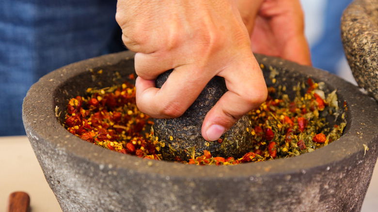 A hand grinds ingredients in a stone molcajete