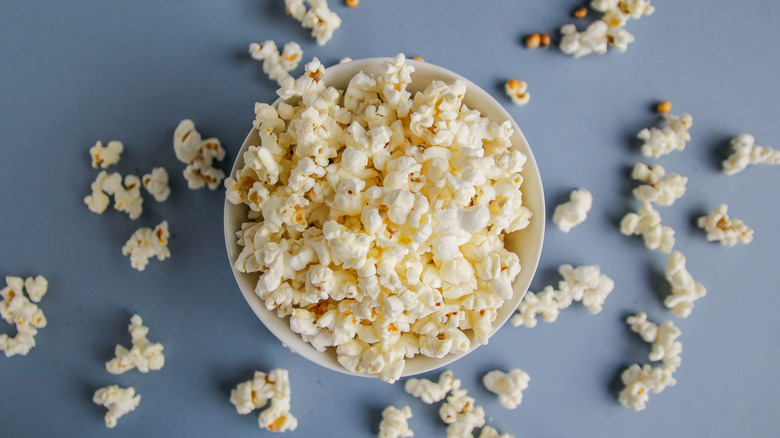 A bowl of popcorn with kernels scattered in the background