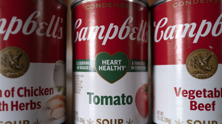 A can of Campbell's Heart Healthy Tomato soup between two additional cans, one cream of chicken with herbs and the other vegetable beef.