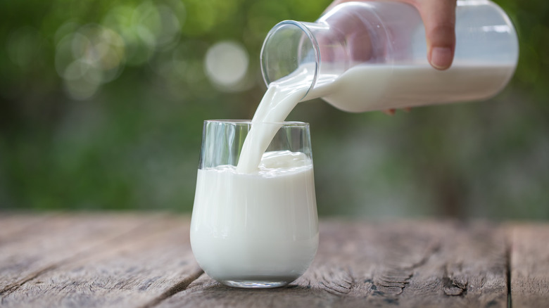 A hand pouring milk into a glass on an outdoor wooden table