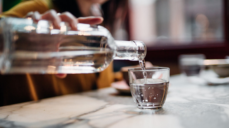 A person pouring water into a glass from a glass bottle in a restaurant