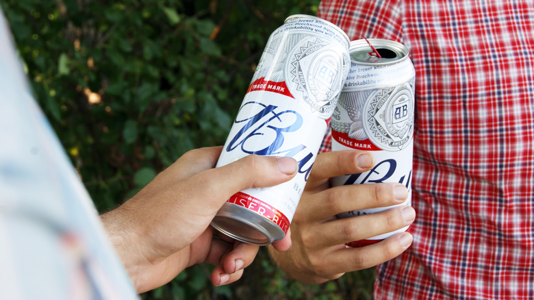 Two people toasting Budweiser cans with one another