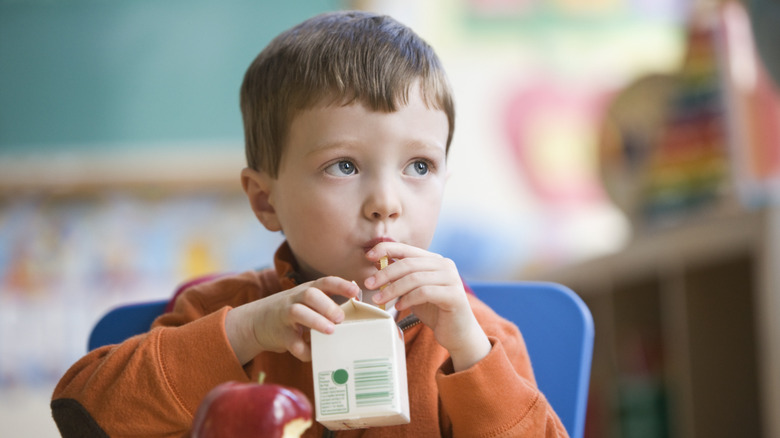 A young boy sips juice from a carton