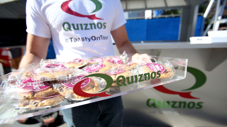 Someone in a Quiznos shirt holding a tray of Quiznos cookies