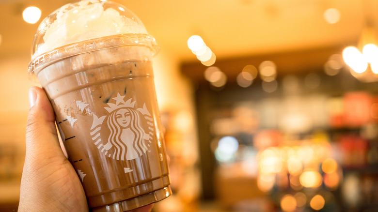 A Starbucks drink being held in front of a blurred Starbucks lobby