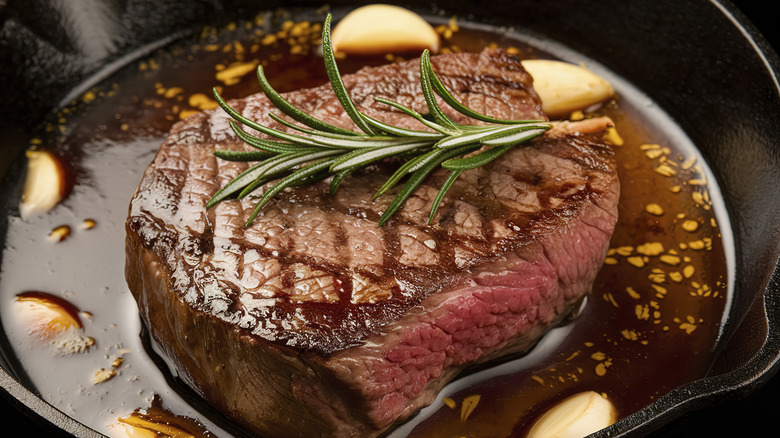 Seared medium rare steak in a cast iron skillet with garlic cloves and jus