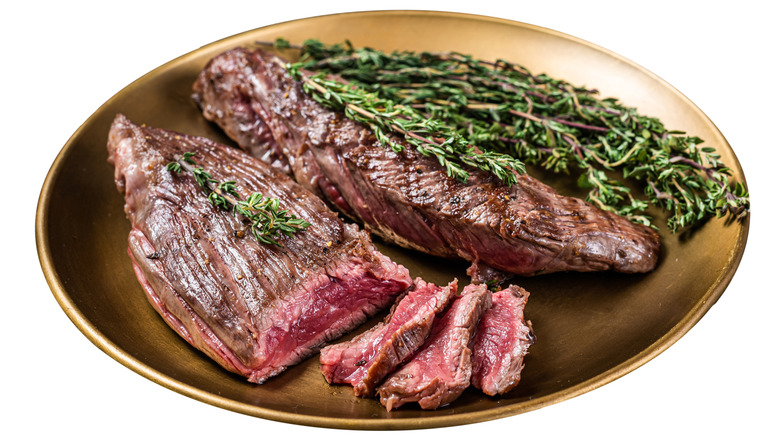 Rare bavette steak on a brown plate with herbs.