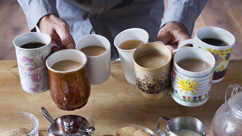 A person holding several cups of coffee over a wood table