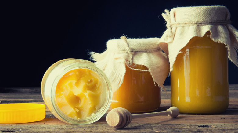 Crystallized honey in jar next to a honey dipper and two honey jars sealed with cloth