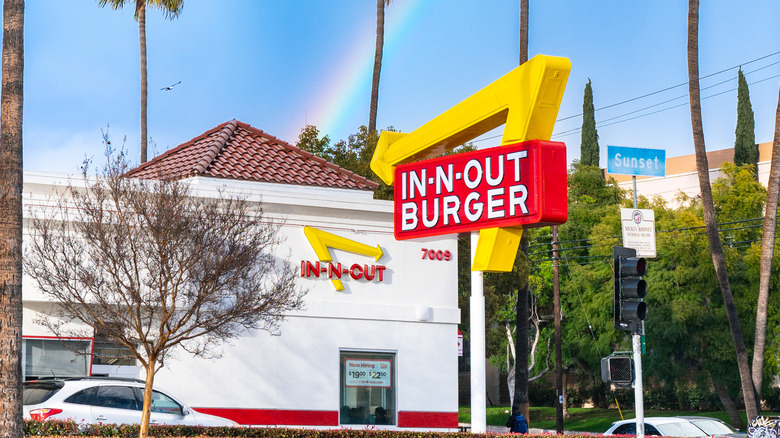 The exterior of an In-N-Out Burger location in California with a rainbow behind it